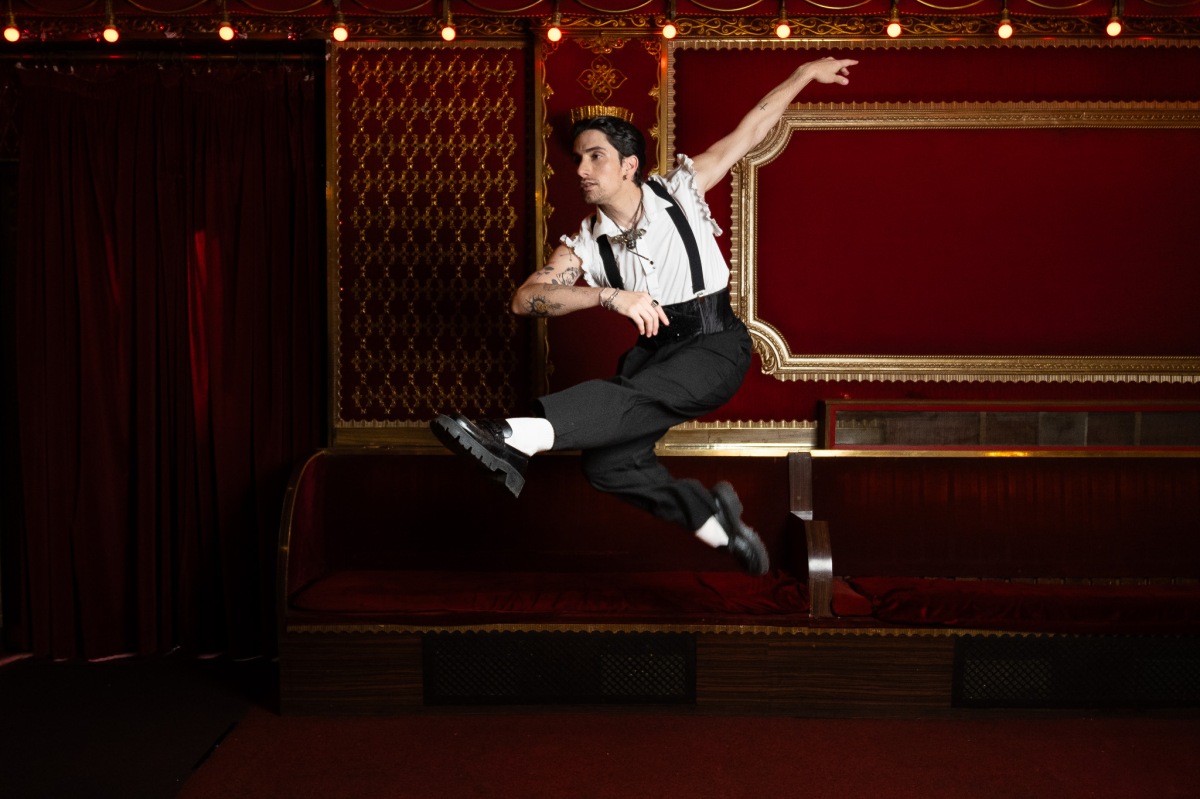 A Male dancer jumping through the air with a red velvet elegant backdrop in a theatre